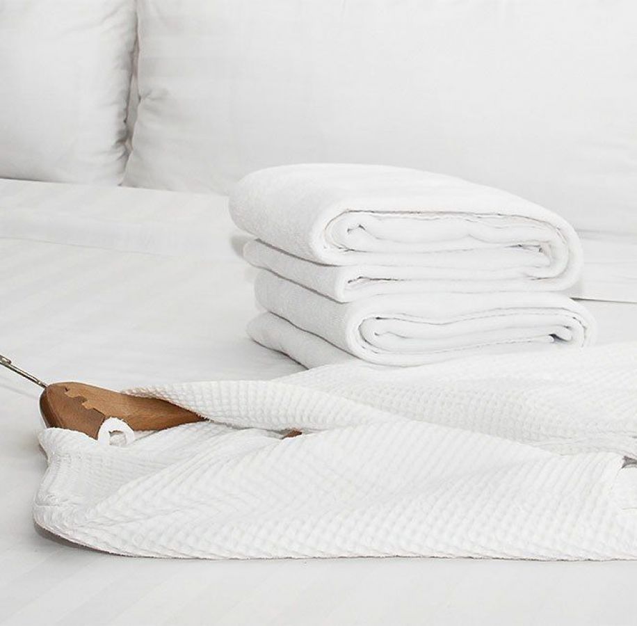 Ein Stapel weißer Handtüscher und ein weißer Bademantel liegen auf einem weißen Bett